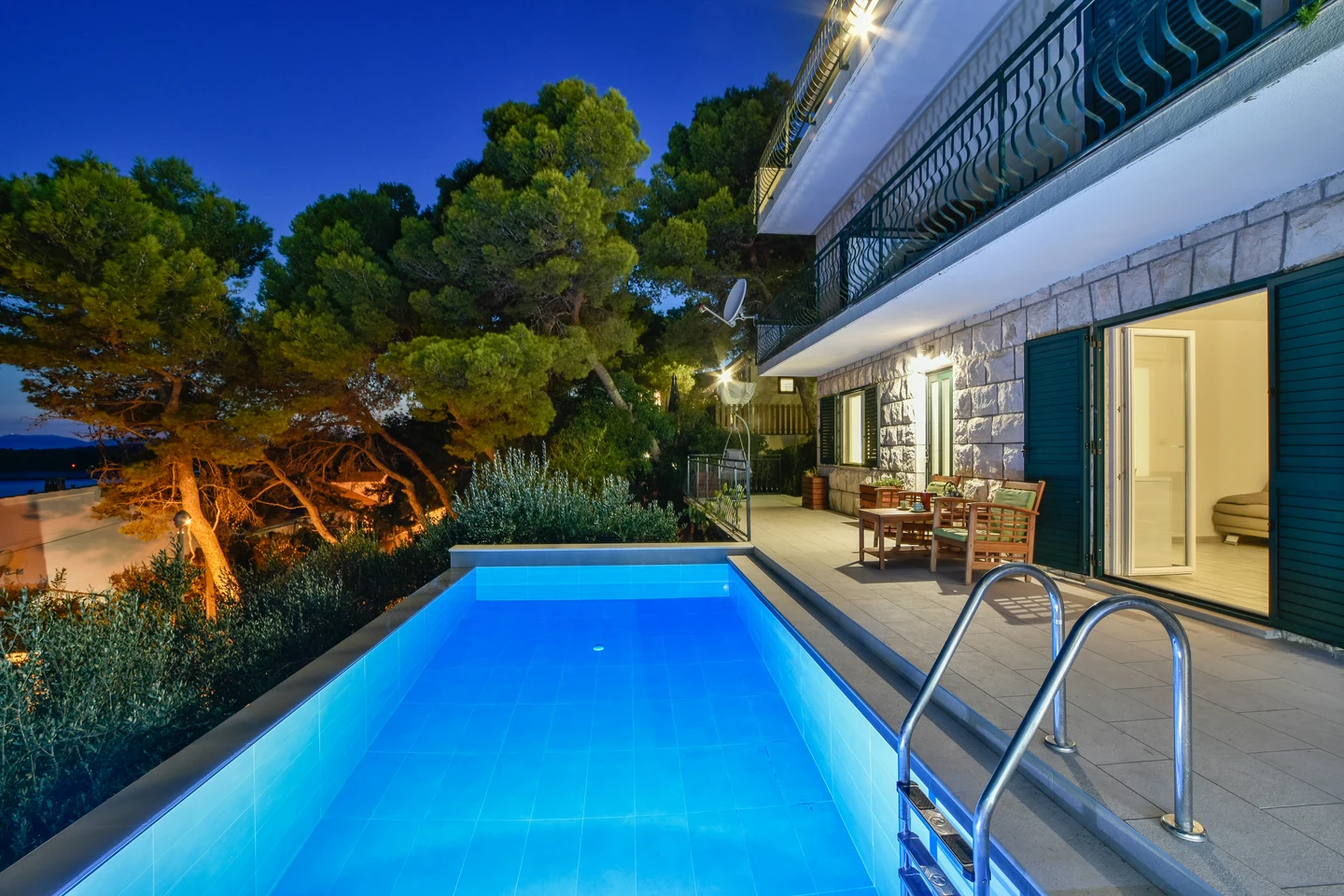 The illuminated pool beside the villa and old pine trees