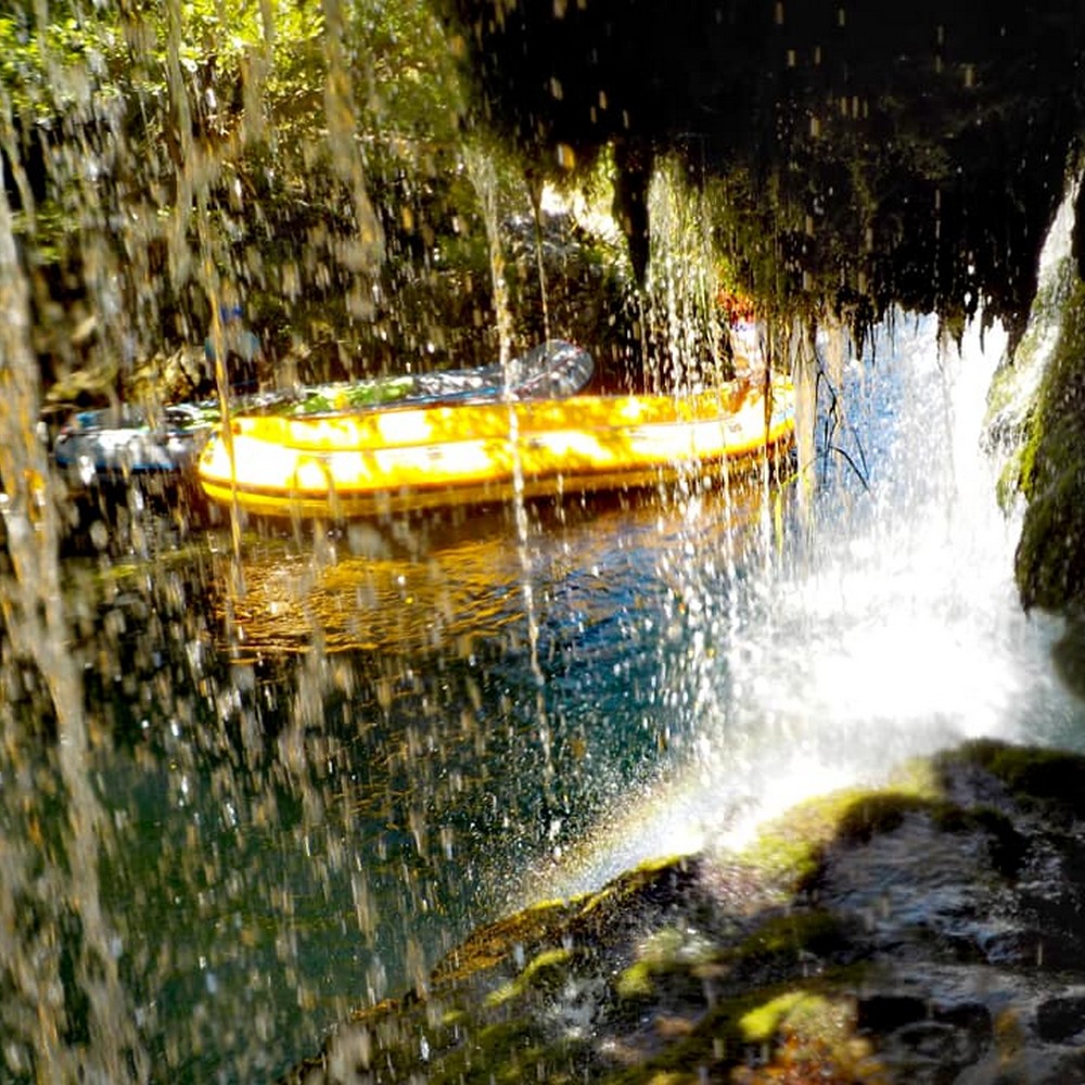 A yellow raft beyond a small waterfall on the river